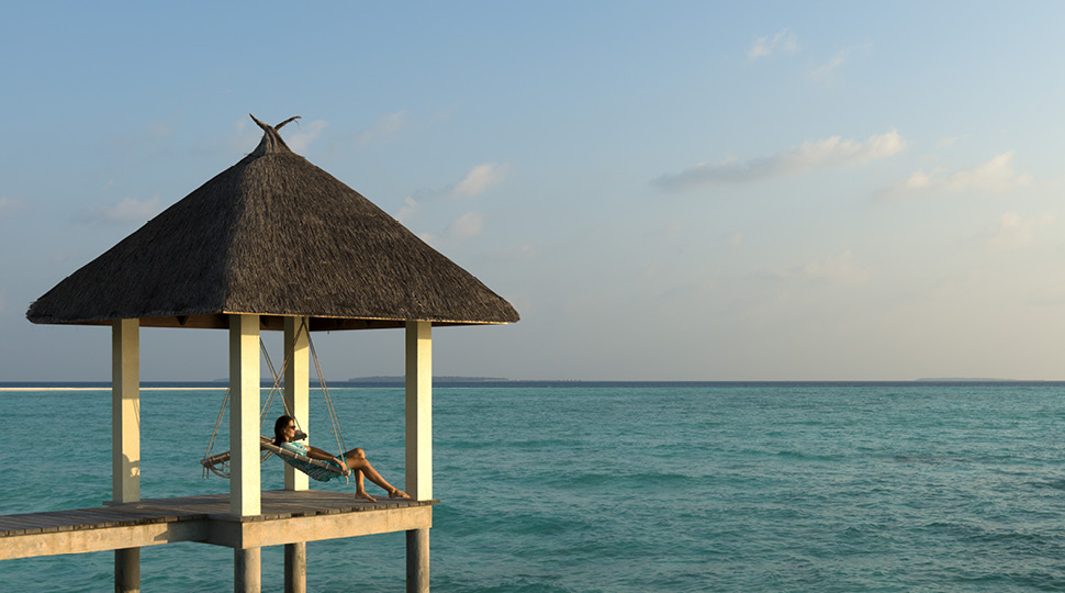 Woman sits in swing under a gazebo overlooking the ocean