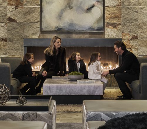A family sits in a living room with a fireplace in the background