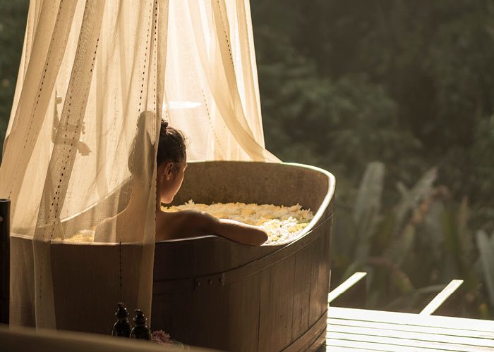 A woman lounges in a canopied bathtub overlooking the jungle