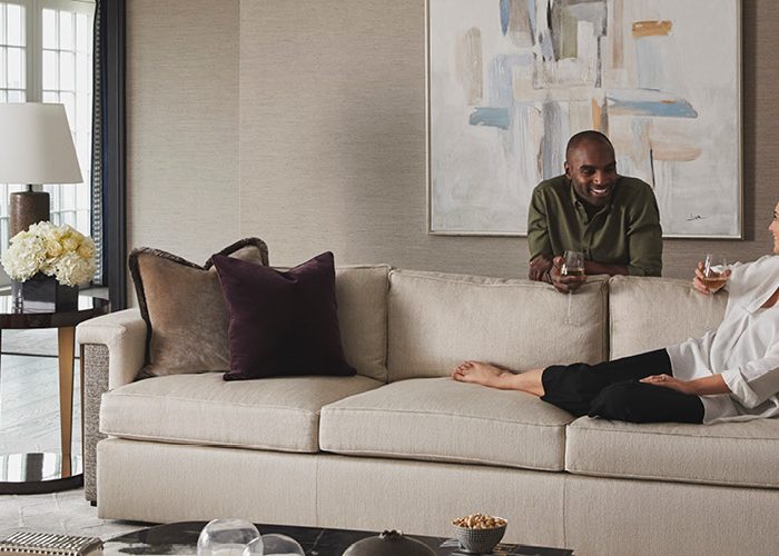 A woman lounges on a tan couch as a man leans on the back