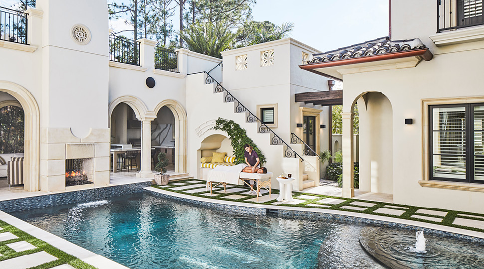 A woman is given a massage on a massage table on an outdoor pool patio