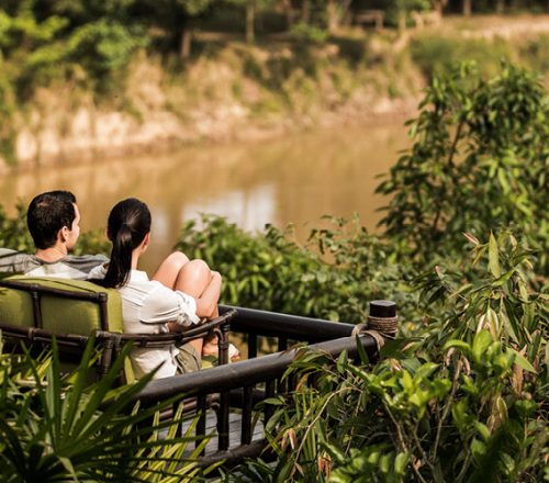 A couple sits on an outdoor couch overlooking the jungle