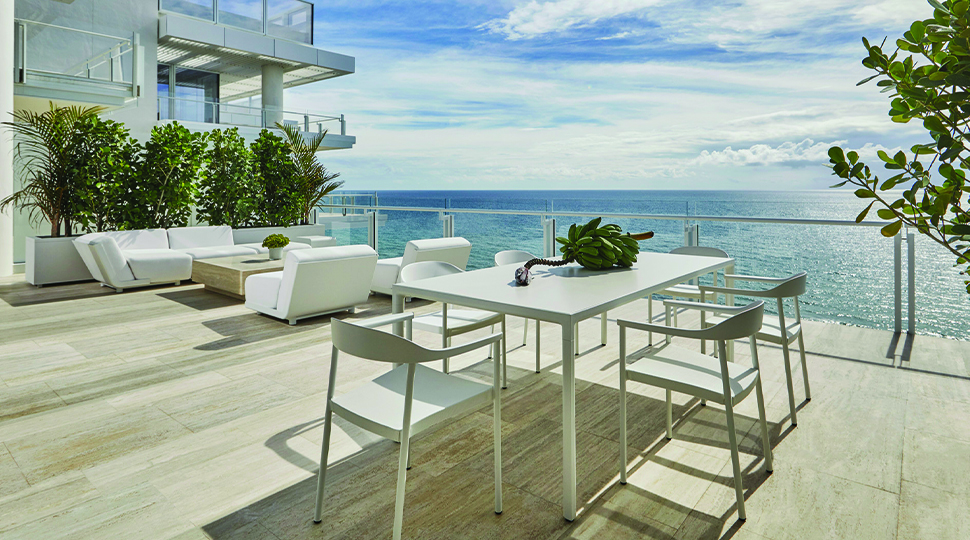 Outdoor terrace with dining table and chairs and lounge area with white outdoor sofas overlooking the ocean