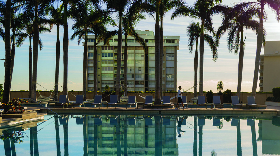Outdoor pool rimmed with palm trees with skyscrapers in the background