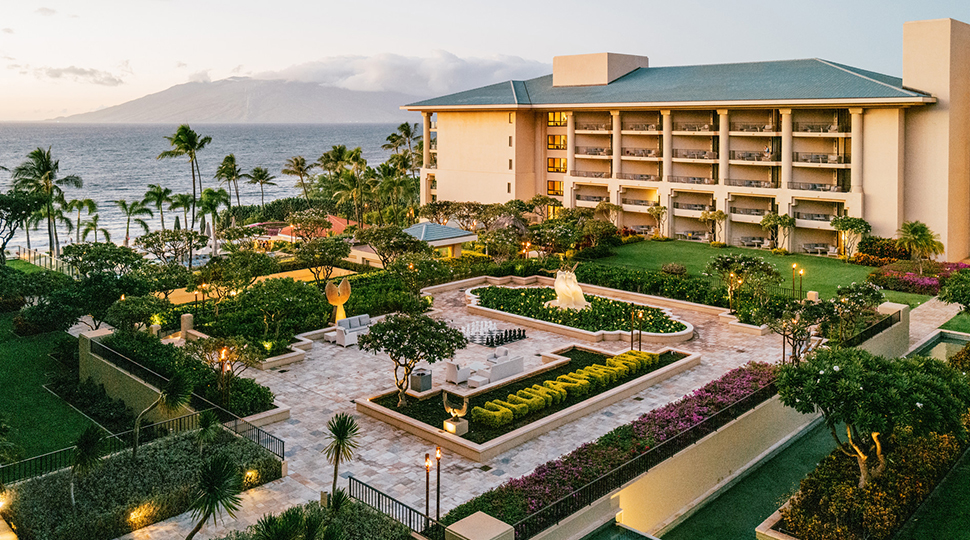 Aerial view of landscaped courtyard with tile walkways and manicured green hedges with resort building and palm trees in the background