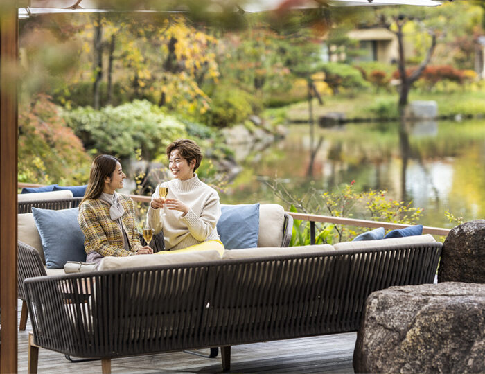 Two people sitting on an outdoor sofa, enjoying drinks by a tranquil pond garden at Four Seasons