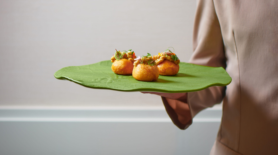 Waiter holds a green platter with three servings of food
