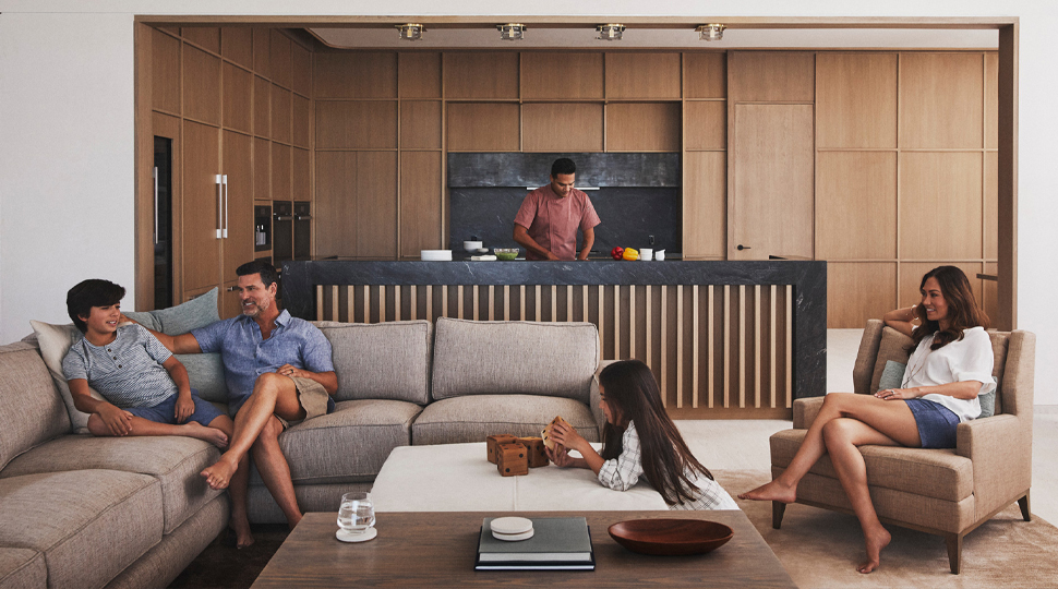 Family of four relaxed in living room while chef prepares meal in open kitchen