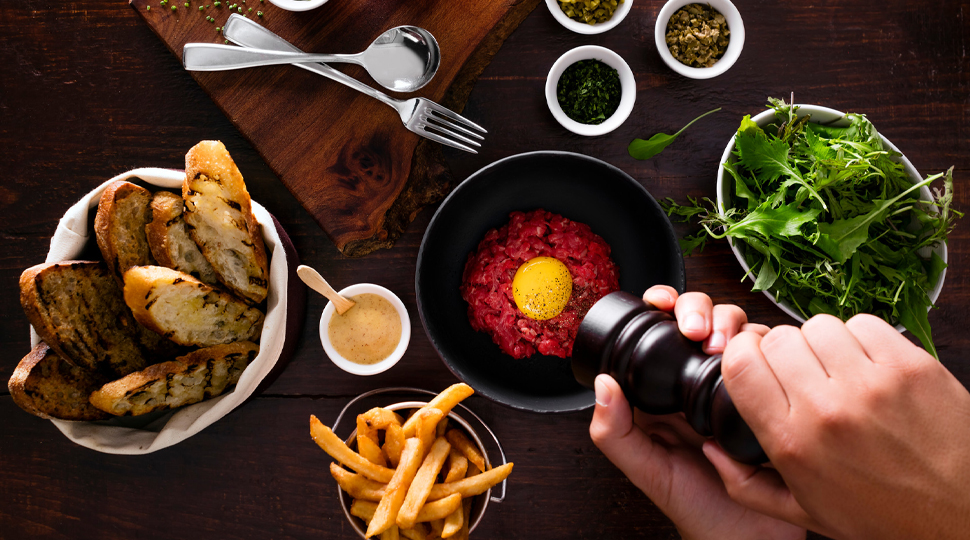 Overhead view of hand grinding pepper into a bowl with various other bowls of food nearby