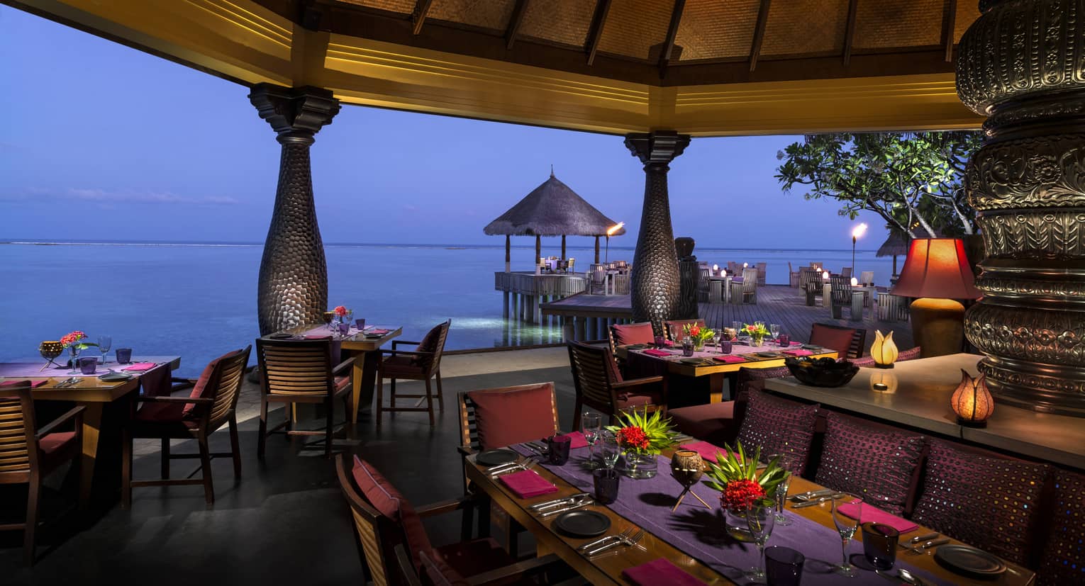 Evening view of Baraabaru restaurant dining patio on the water, with tropical flower arrangements, lanterns