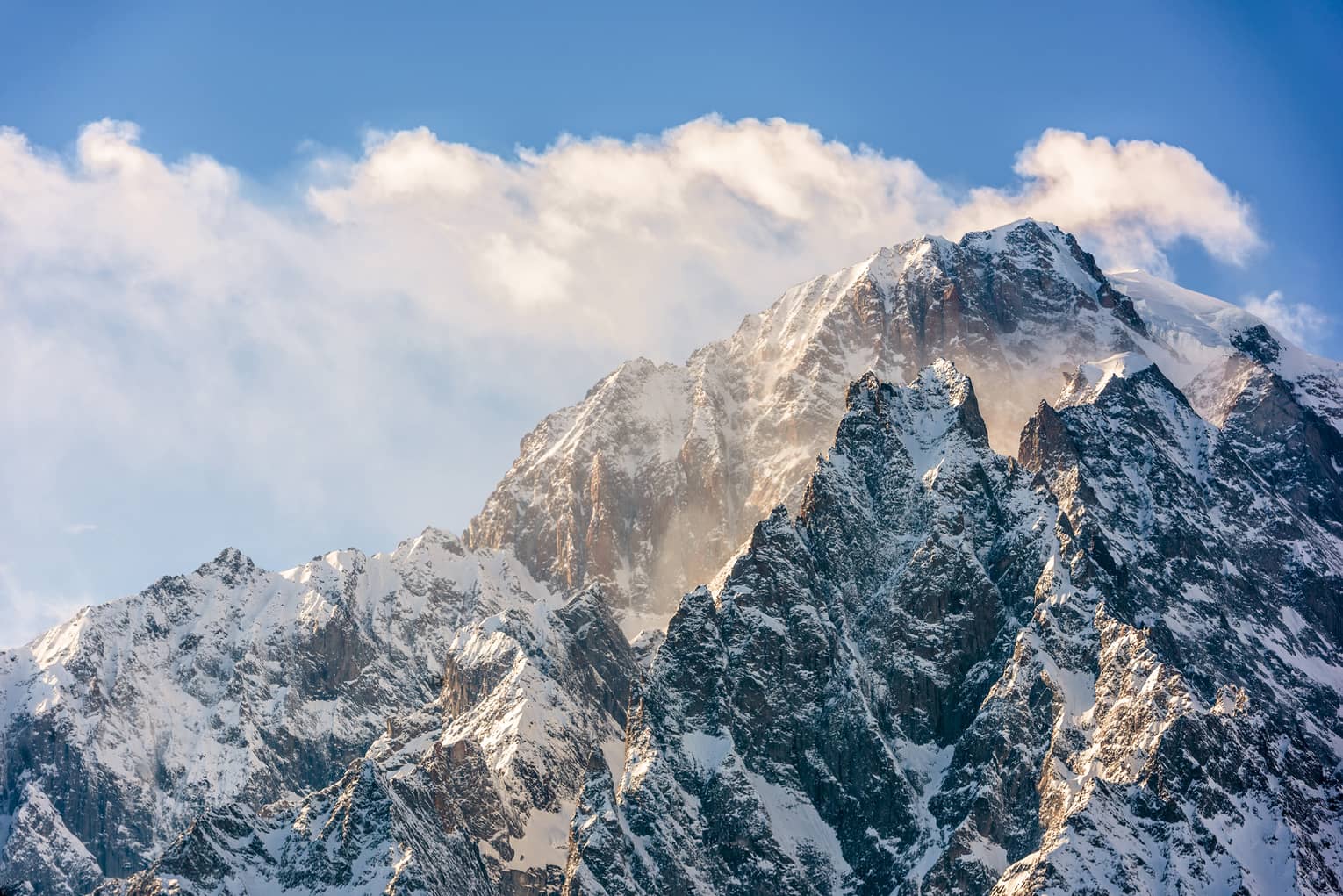 Snowy mountain peaks with blue sky and clouds in backdrop