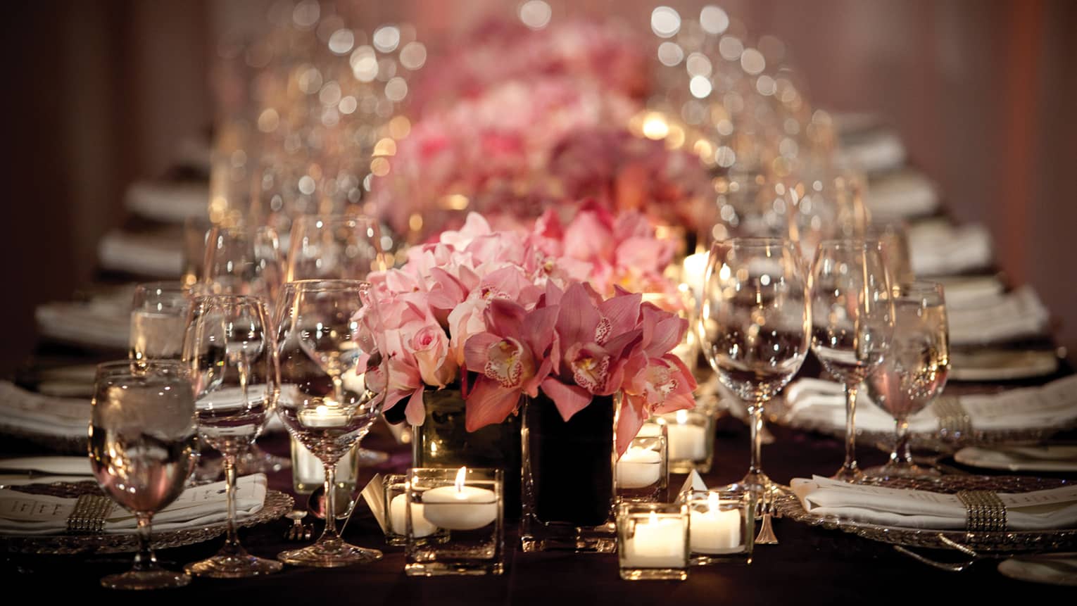 Pink roses, empty wine glasses and glowing candles line long dining table