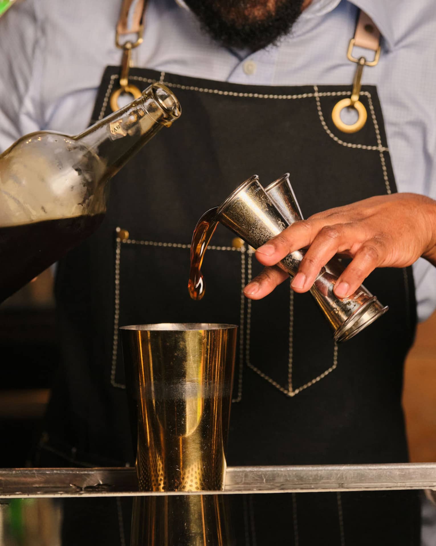 A bartender pours liquid from two jiggers into a cocktail shaker