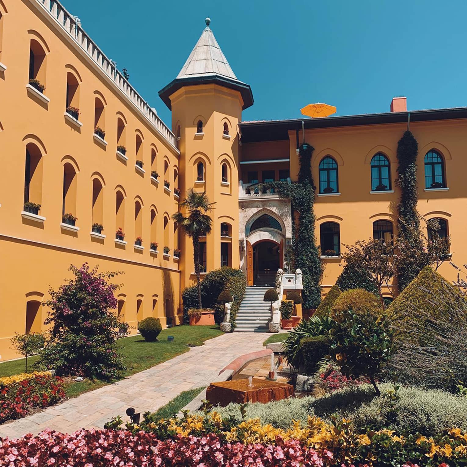 Garden courtyard under hotel building with turret, blue sky