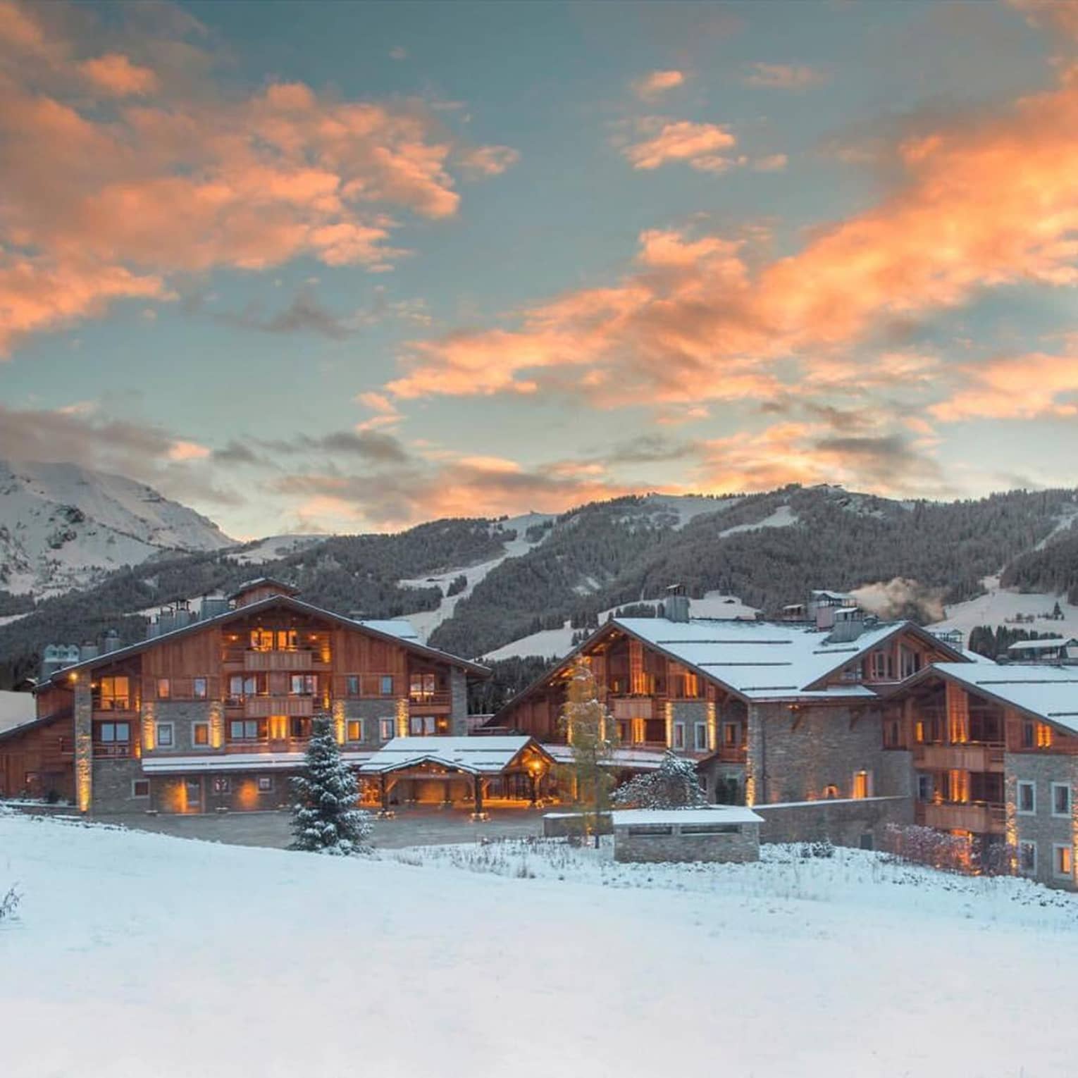 Four Seasons Hotel Megeve lodge with lights on snow-covered mountain at sunset