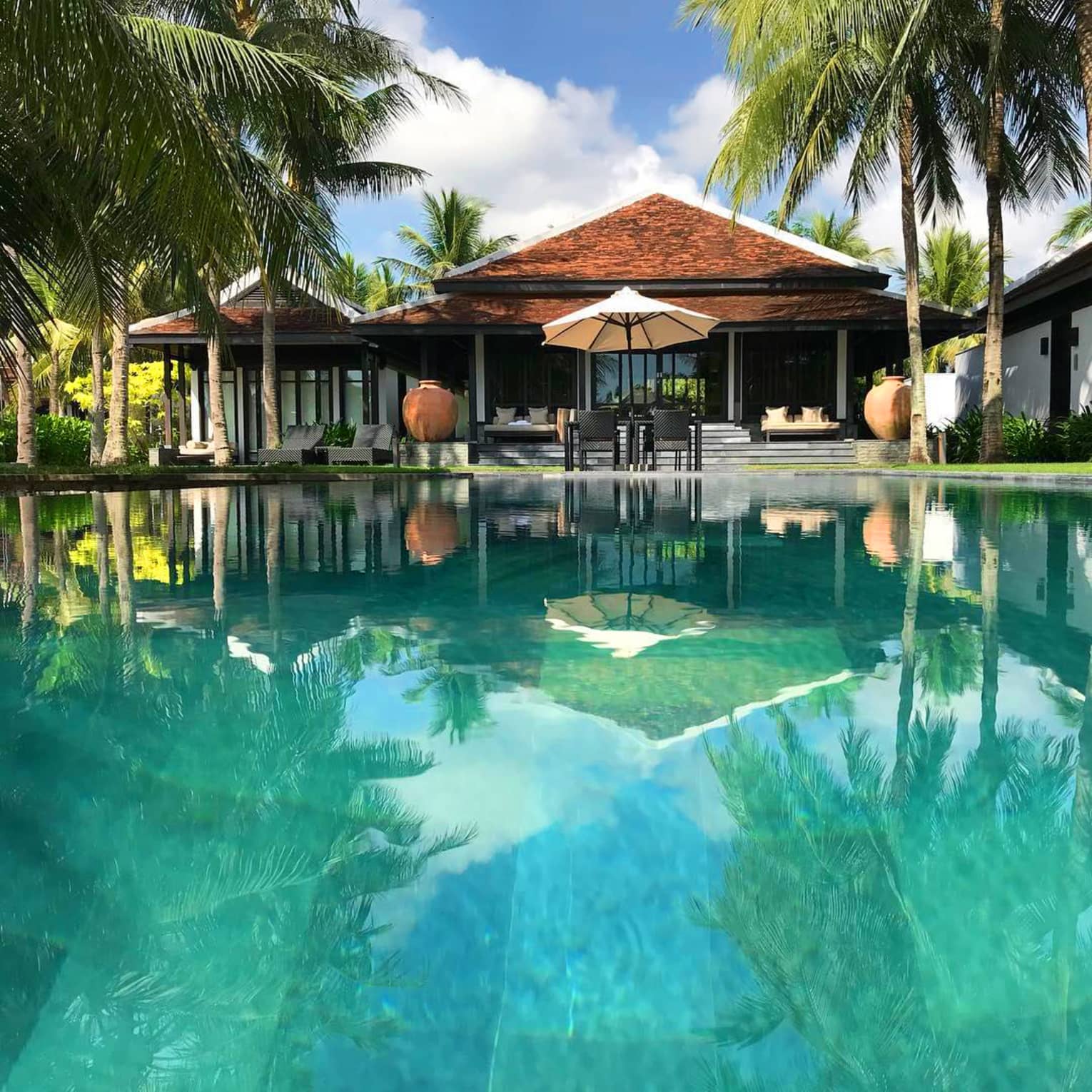 Reflections of villa, patio, umbrella on turquoise water of pool