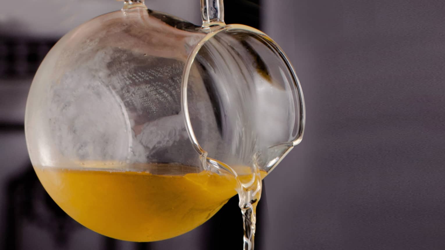 Hot tea in a glass pitcher being poured into a chilled glass dish filled with flower petals