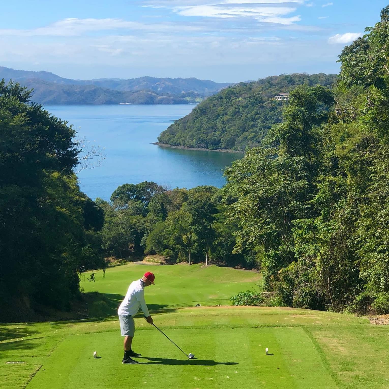 A guest prepares to hit a golf ball from a tee on a course with stunning Costa Rican water views