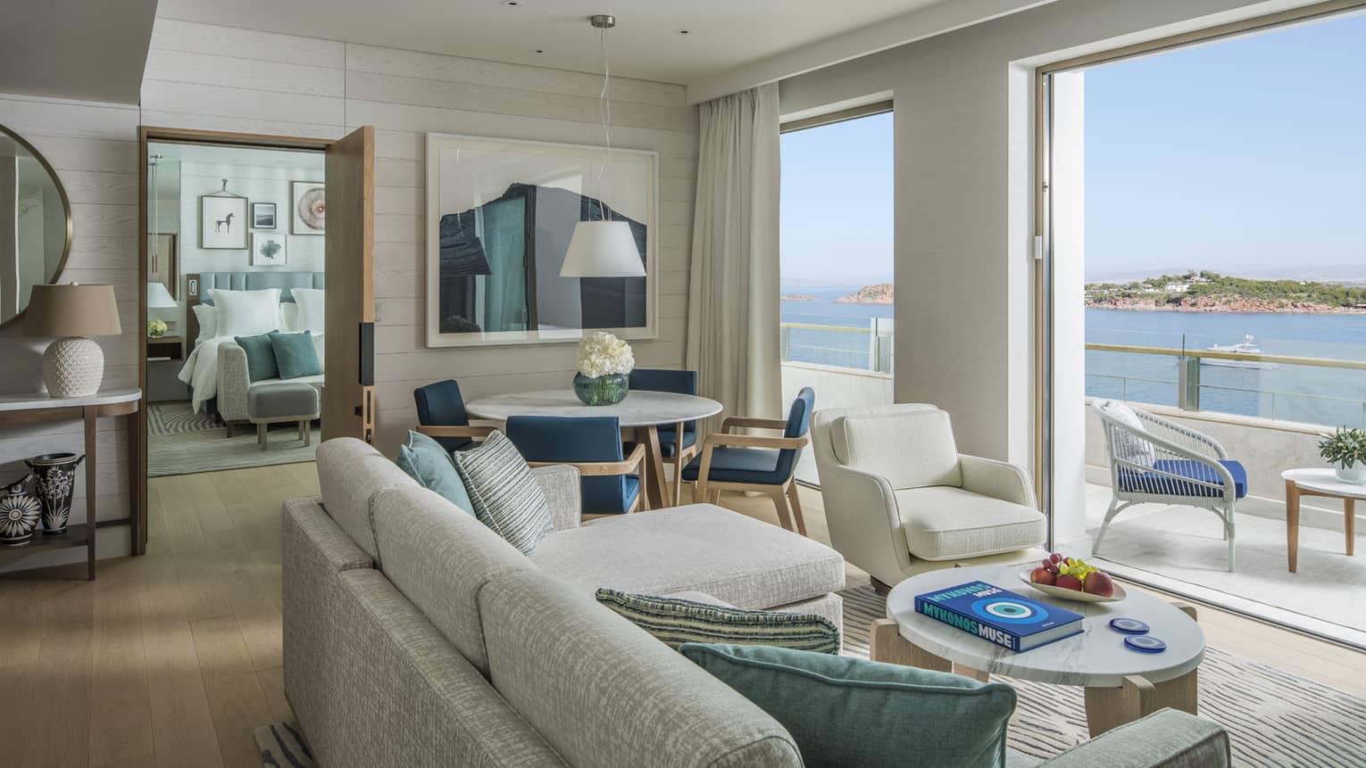 Light-filled living room with off-white sofa and arm chair, plus dining area, looking out to sea