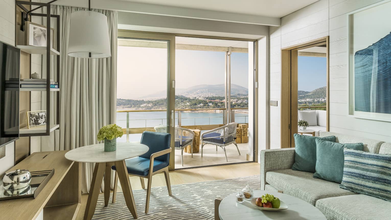 Arion Corner Suite with cream sofa, blue accent pillows and wall art, oval coffee table, round table for one, sliding glass doors leading to balcony, ocean views