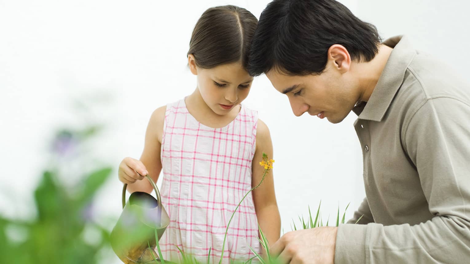 Man and young girl with watering can in tall grass, garden
