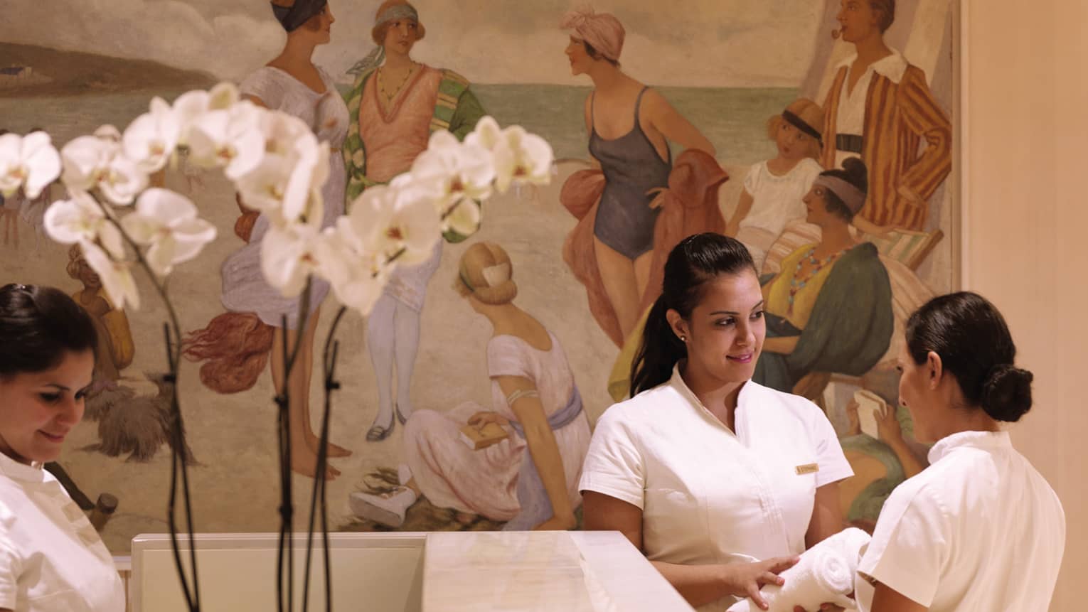 Spa staff at desk with large mural, white orchids