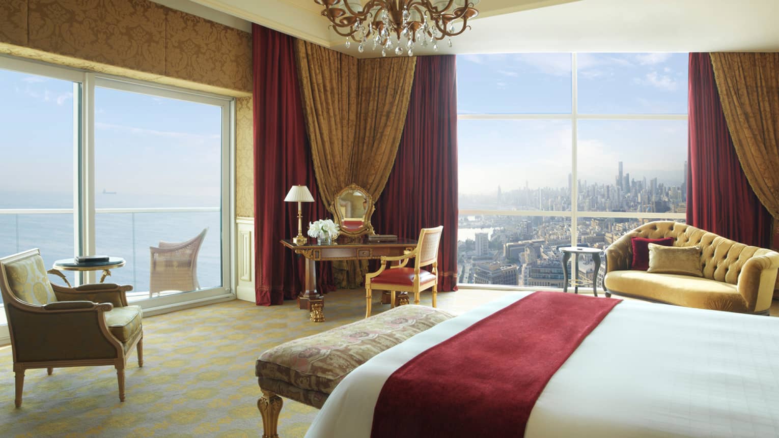 White bed with red suede sash, antique-style bench, green-and-gold leaf armchair, corner suite views of water and city