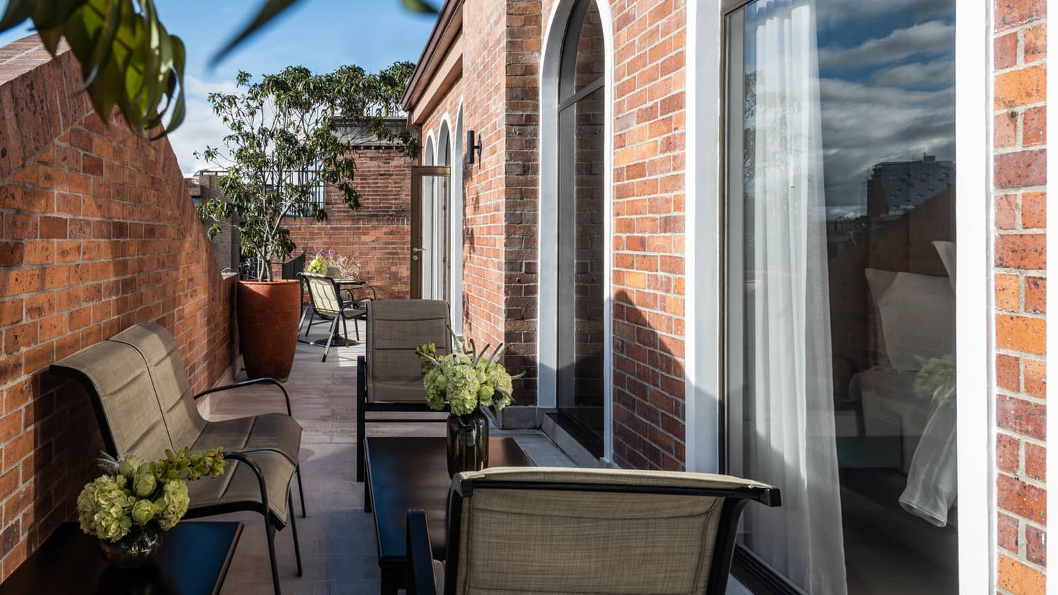 Outdoor terrace off guest room with matching coffee table and end tables, lounge chairs, large potted palm