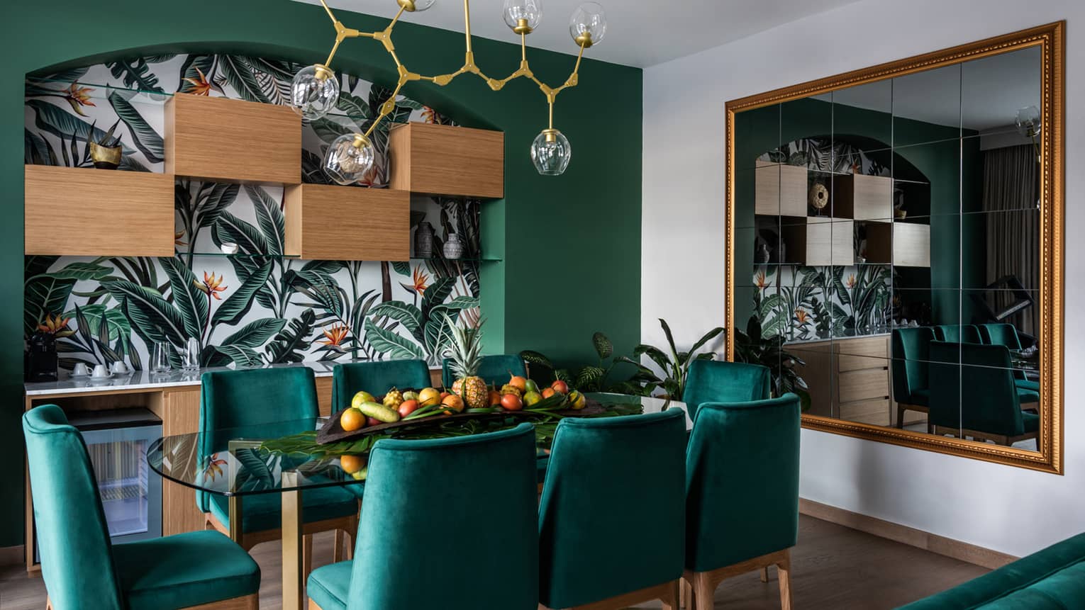 Dining room with rectangular glass table and eight kelly green chairs, green accent wall with island wallpaper, large mirror