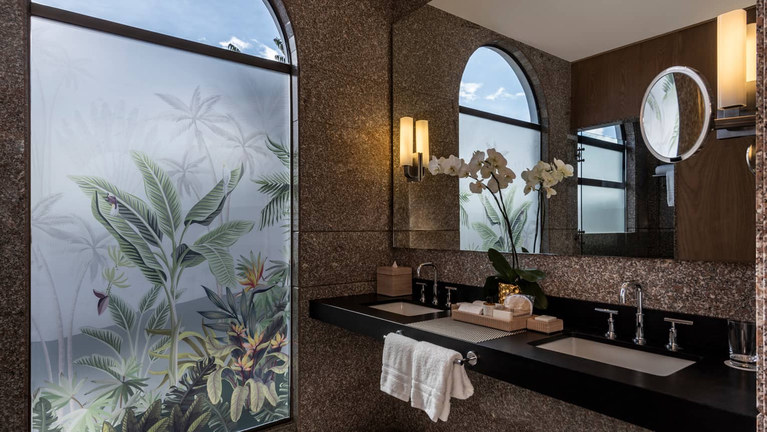 Bathroom with double vanity and sinks, full-width mirror, lighted wall sconces, patterned frosted glass shower door