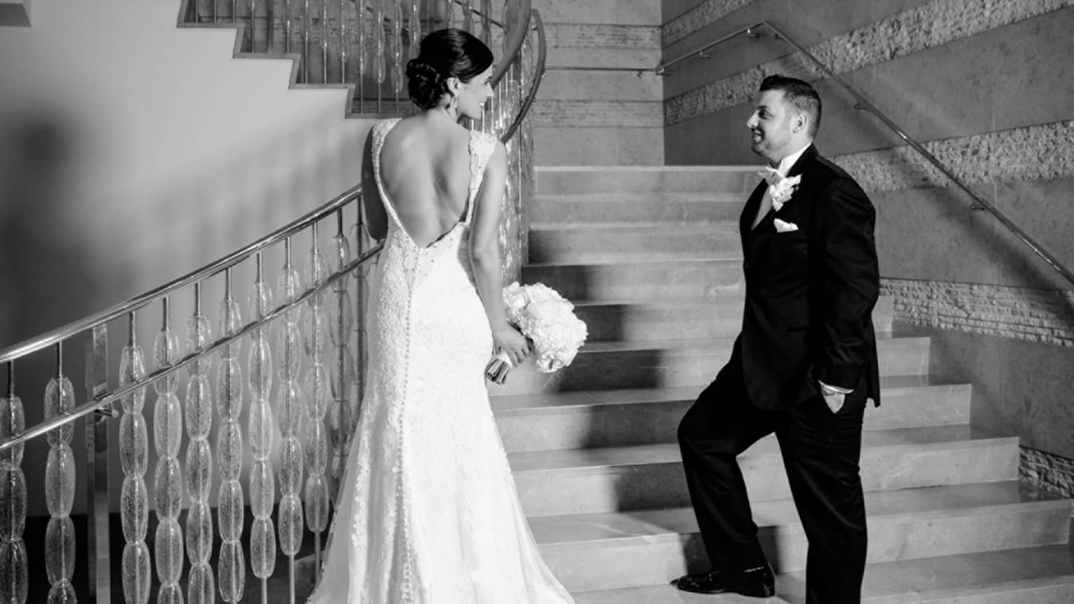 Black and white photo of groom and bride with long gown at bottom of staircase