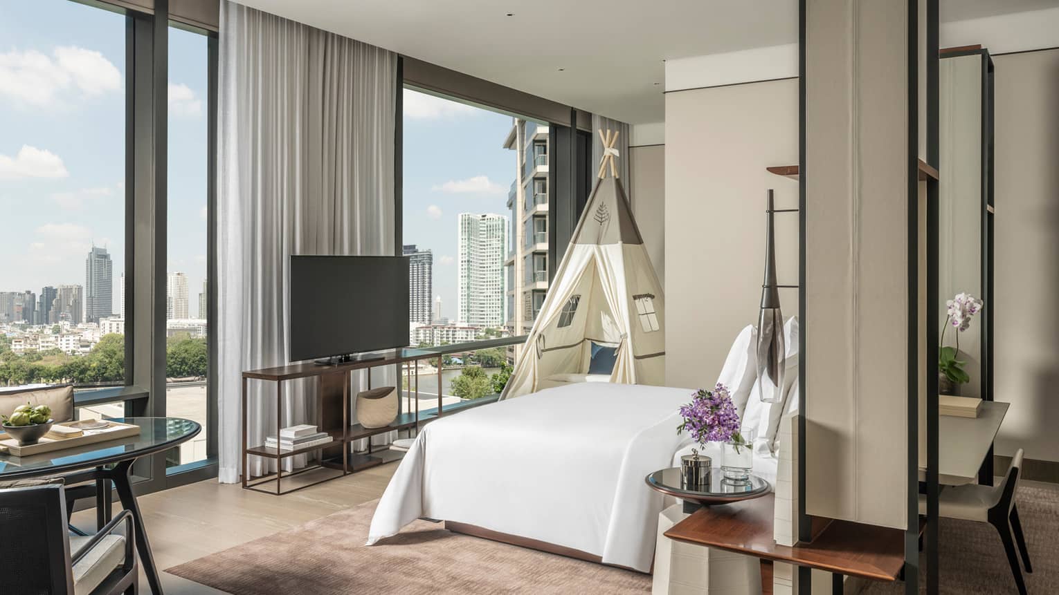 Studio hotel suite with a king bed, wall of windows, TV and a kid's teepee
