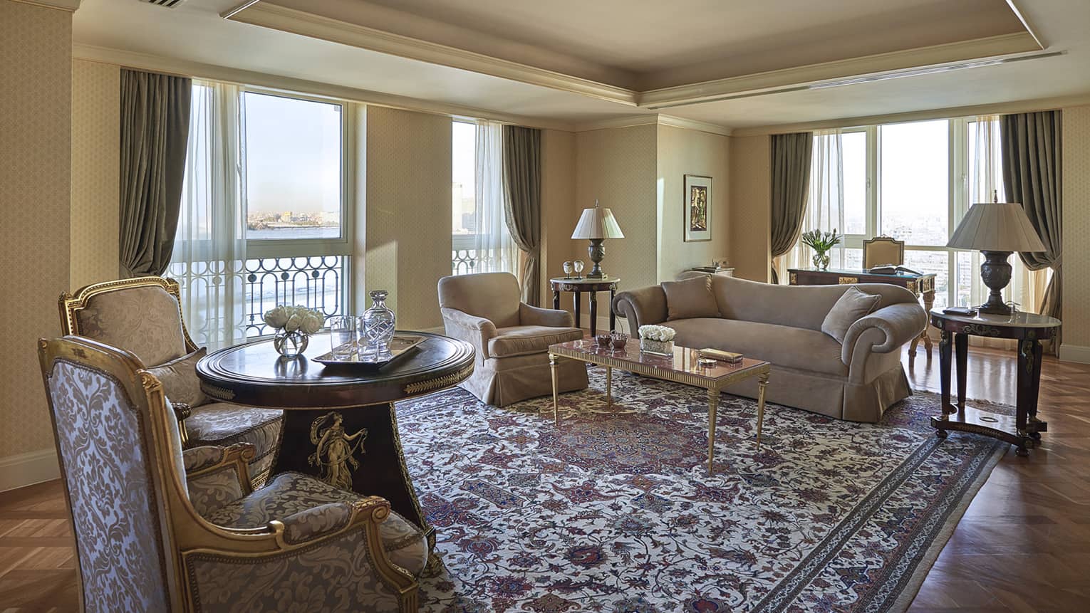 Presidential Suite living room with antique-style armchairs, floral area rug, corner windows 