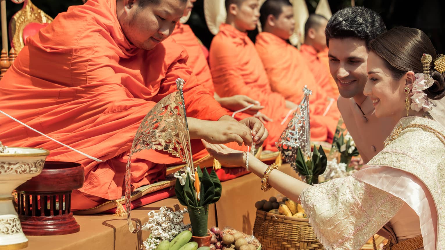 Bride and groom at traditional Thai wedding ceremony, monk ties bracelet around woman's wrist