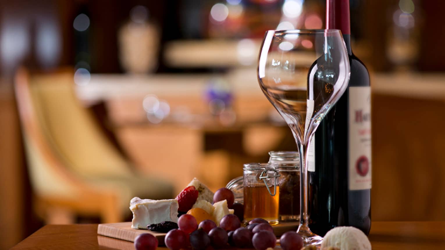 Large empty wine glass next to bottle of red wine, fresh grapes and cheese on counter