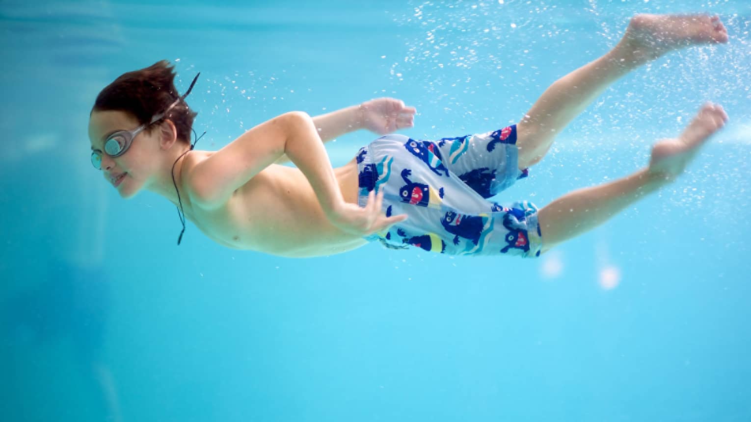 Underwater shot of a boy swimming in a pool with goggles and swim trunks