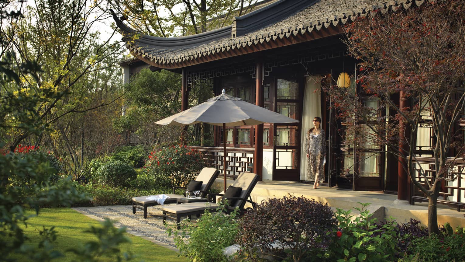 Woman walks out villa door to patio, two lounge chairs under umbrellas