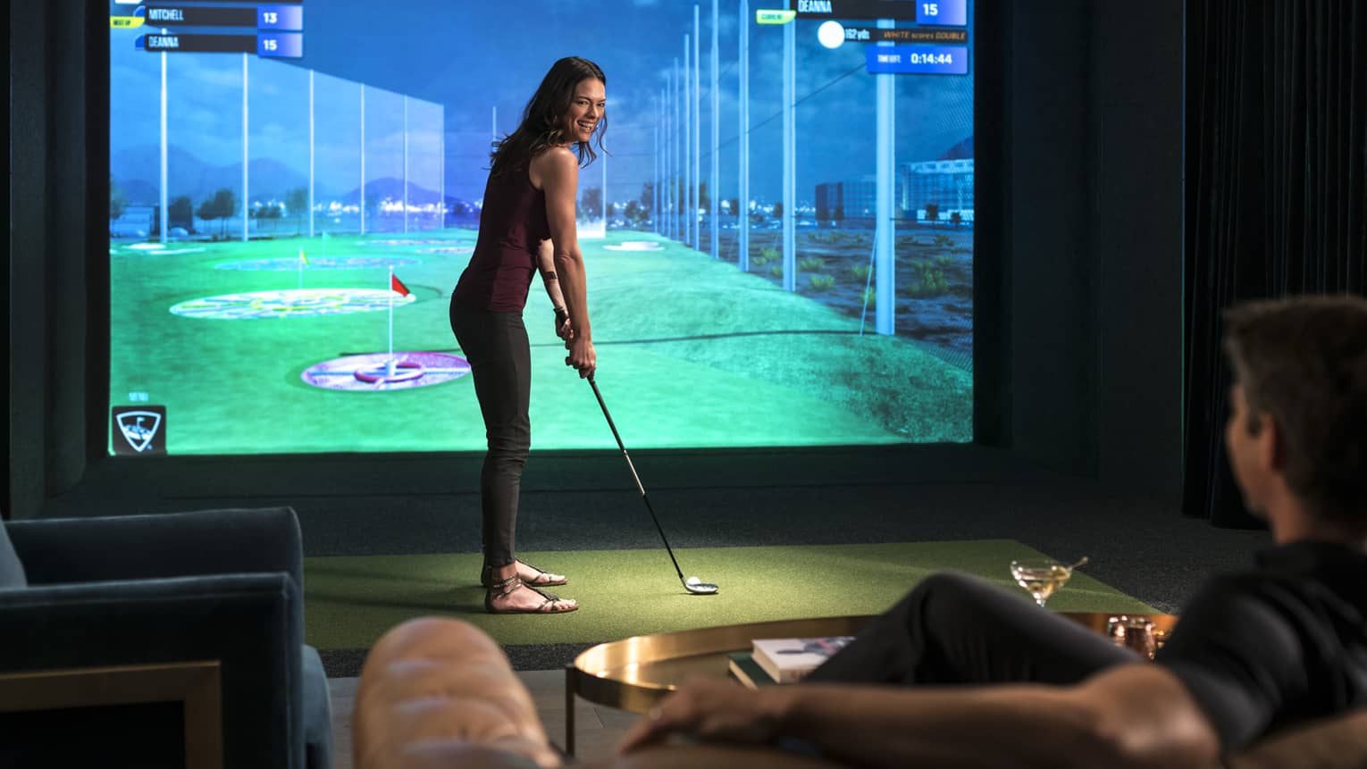 A woman prepares to swing a golf club in front of a virtual golf simulator screen