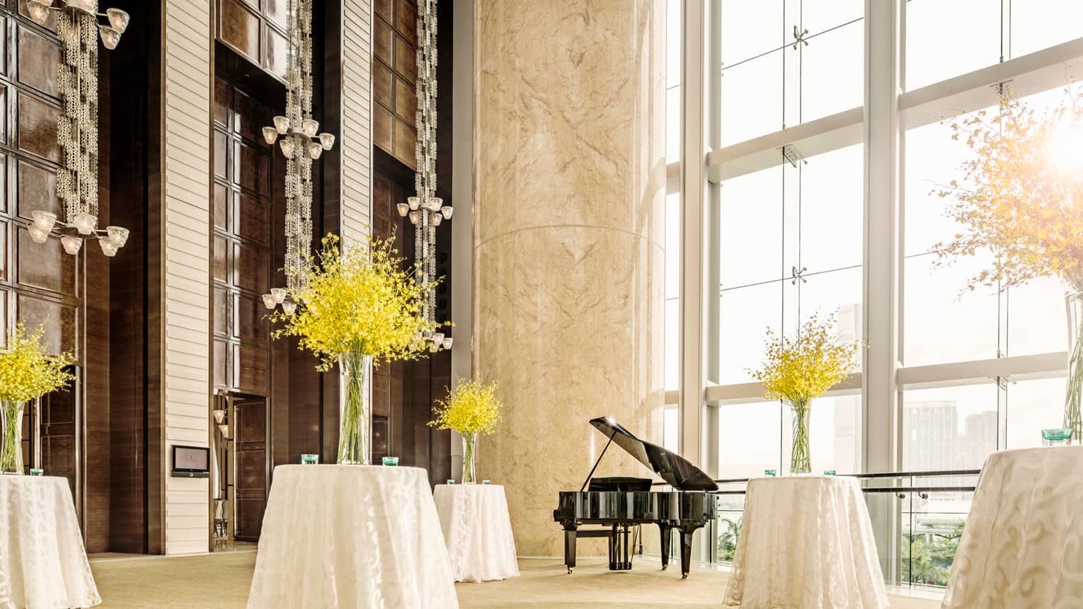 Small cocktail tables with white linens, yellow flowers under wall of loft windows