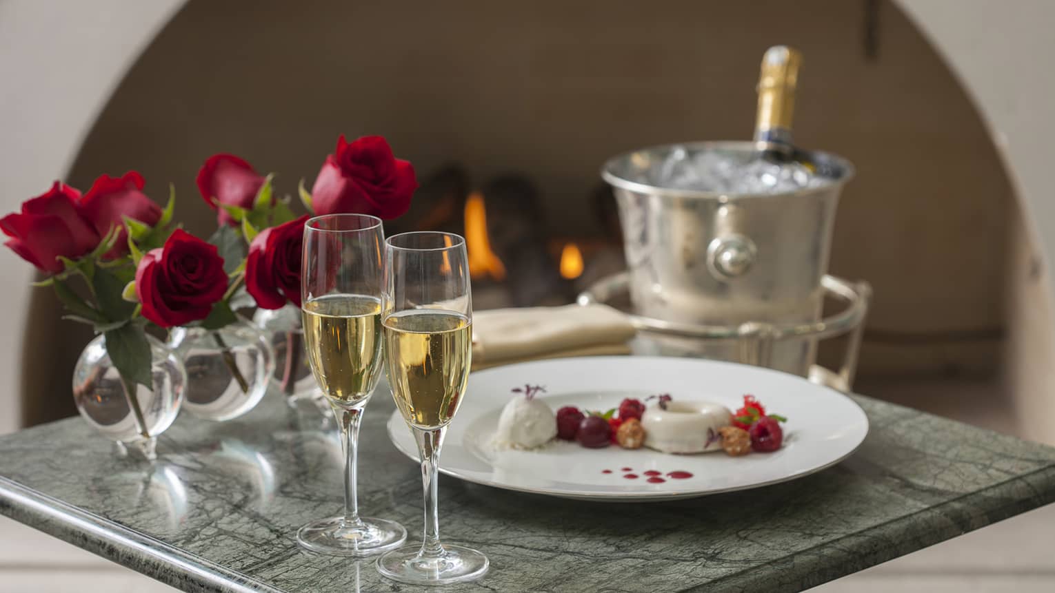 Champagne glasses and bottle on ice, red roses and gourmet dessert on tray