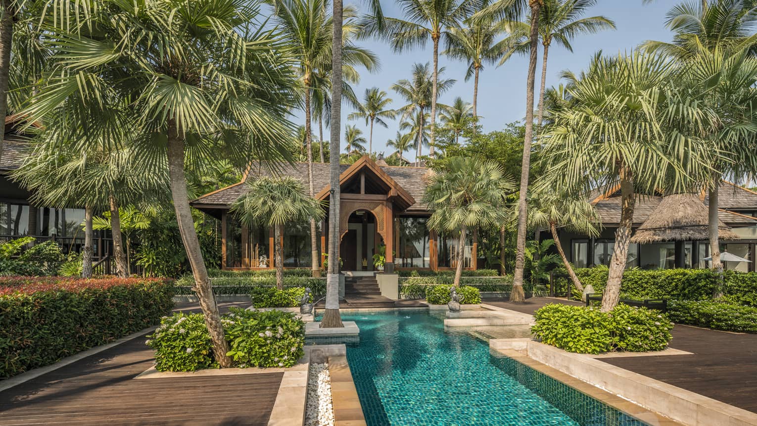 Tall palm trees tower over long outdoor pool, sunny patio