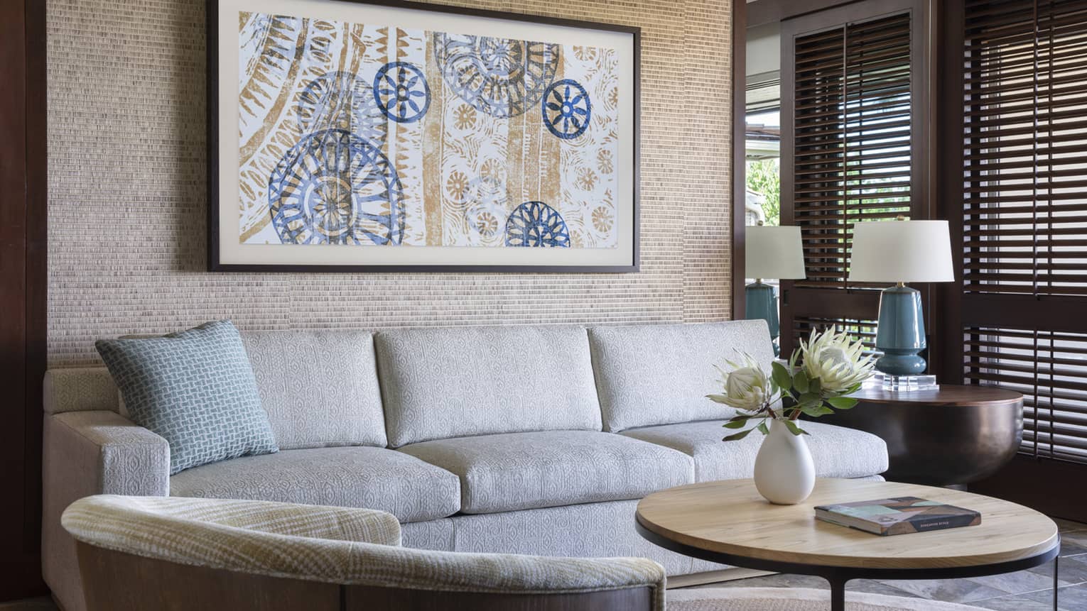 Living room with beige sofa, arm chair, round coffee table, artwork on wall, lamp