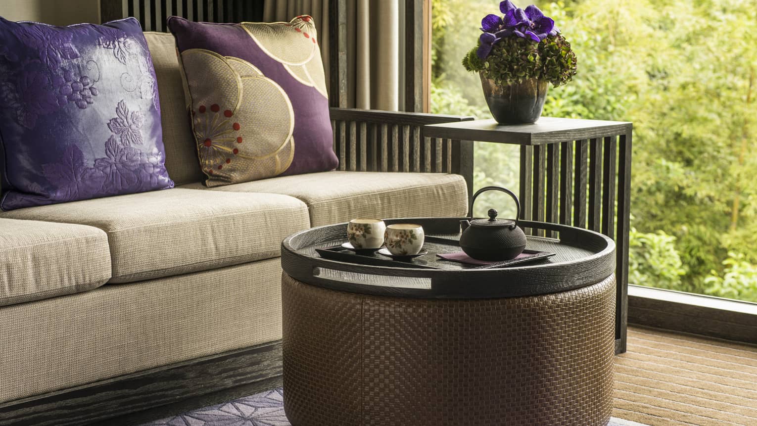 Close-up of beige sofa with purple pillows, round coffee table, garden view out window