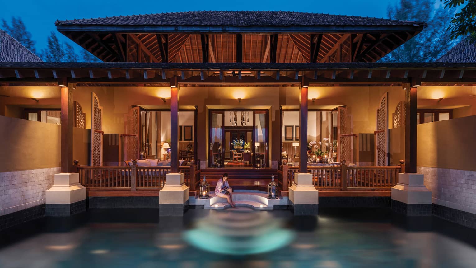 Woman sits on edge of pool off steps to Family Garden Villa at night