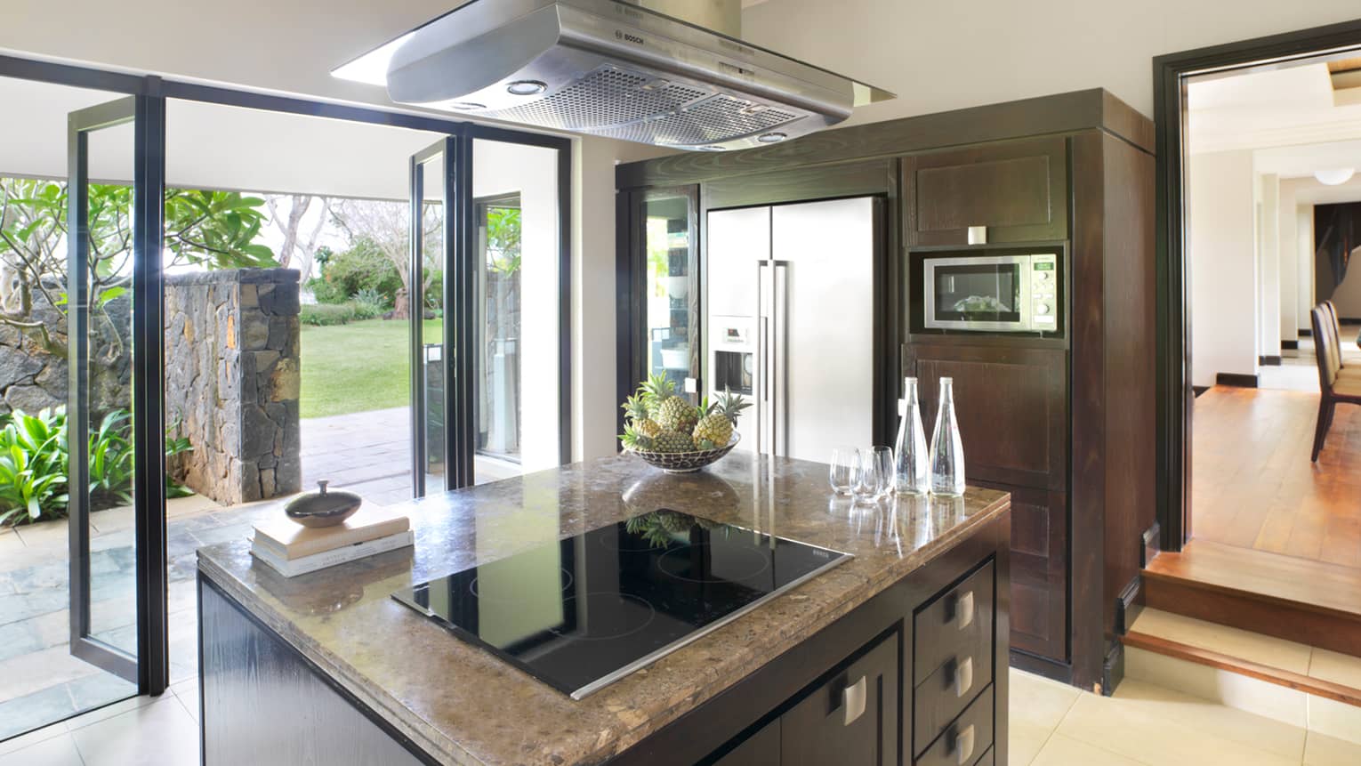 Stove range on marble island in modern kitchen, open glass walls to patio