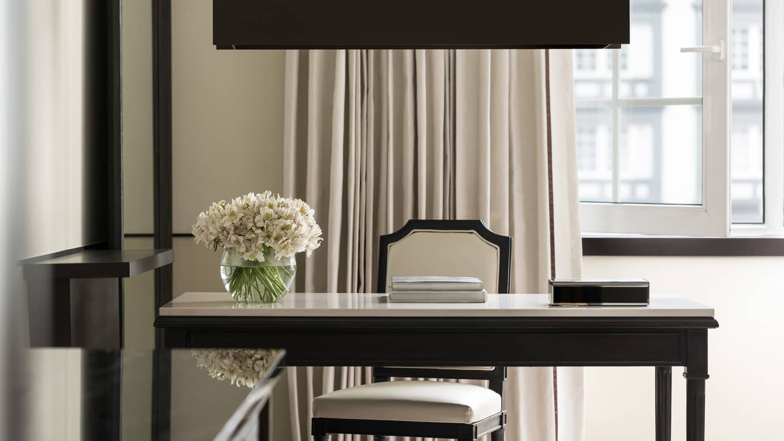 Writing desk with a floral arrangement and upholstered chair by the window