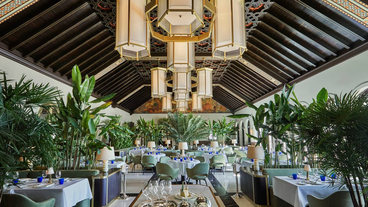 Historic Peacock Alley restored dining room with high ceilings, art deco-style chandeliers and tropical plants