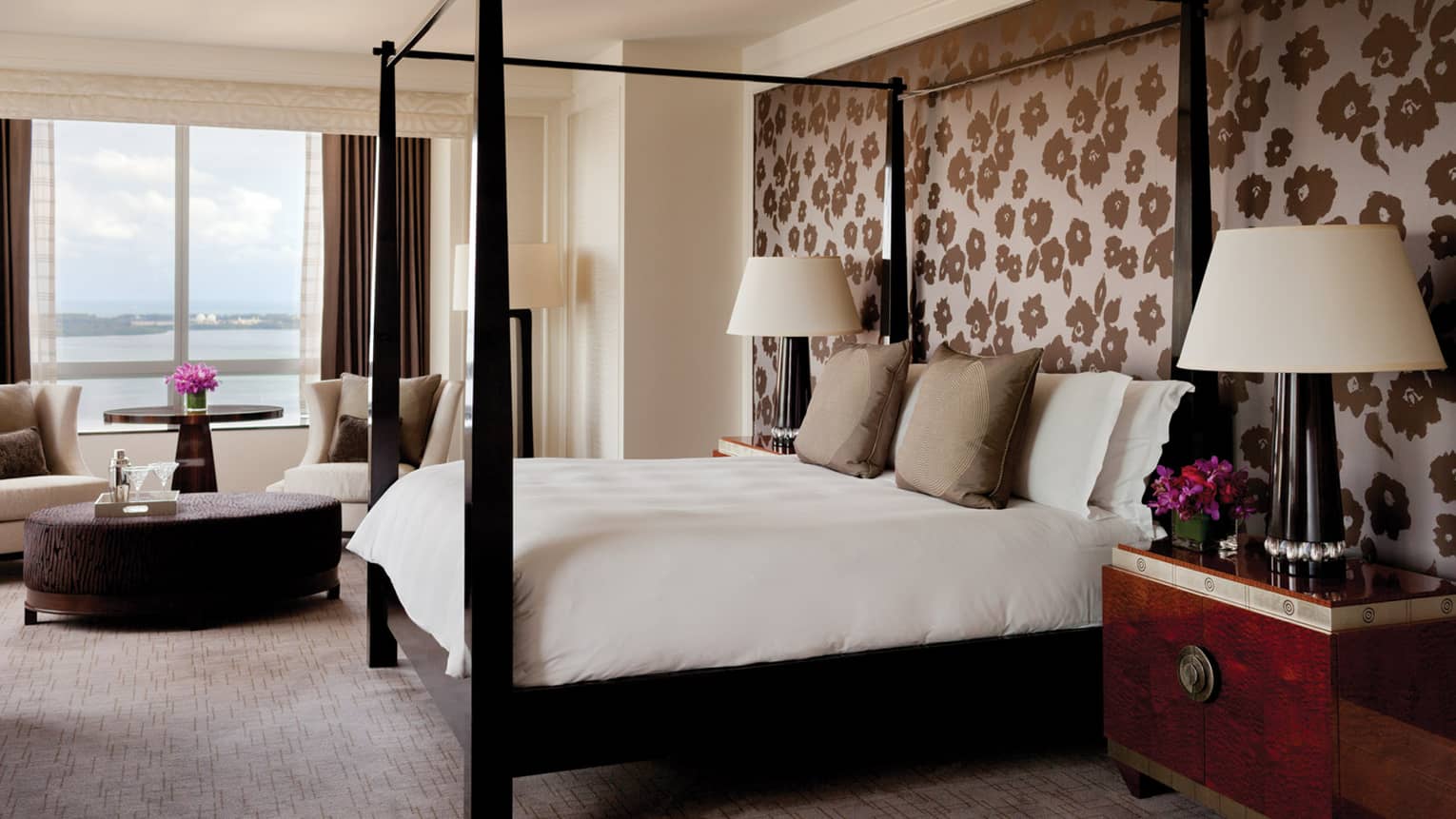 Hotel suite with poster bed against wall with flower patterned wallpaper