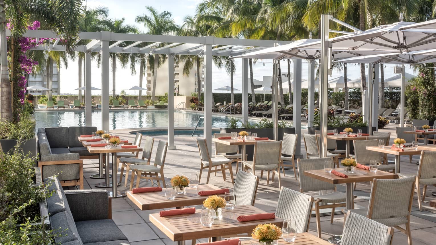 Patio dining tables under white pergolas by swimming pool