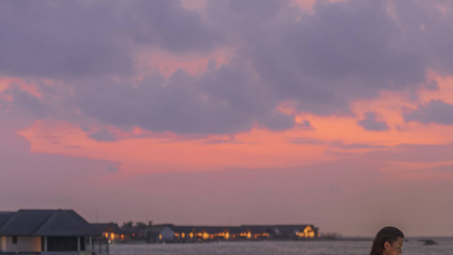 Woman holding cocktail stands at edge of Seabar overlooking the water at sunset